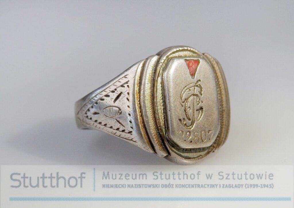 Srebrny sygnet, grawerowany, rzut na oczko oraz fragment grawerowanej obrączki. Zdjęcie wykonane na szarym tle, poniżej znak wodny-logo Muzeum Stutthof.