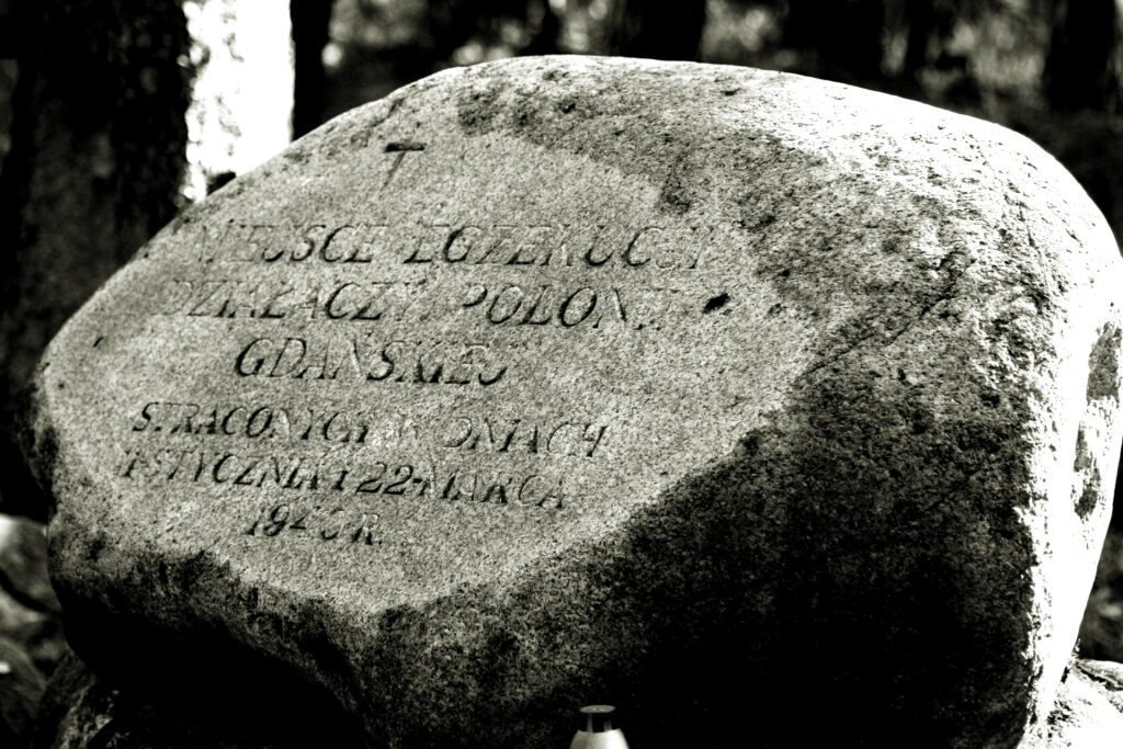 Czarnobiałe zdjęcie przedstawiające kamienień upamiętniający z napisem. Miejsce egzekucji działaczy Polonii Gdańskiej straconych w dniach 11 stycznia i 22 marca 1940 r.