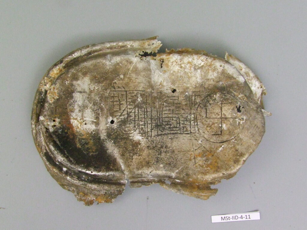 The lid of a mess tin engraved illegally in camp workshops. Condition before conservation.