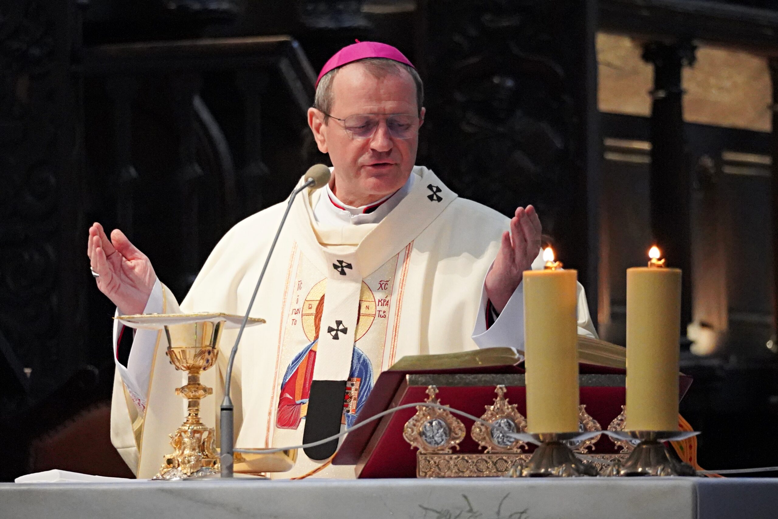 Biskup odprawia mszę, z rozłożonymi rękami, przed nim stoją kielich oraz złote naczynia liturgiczne.