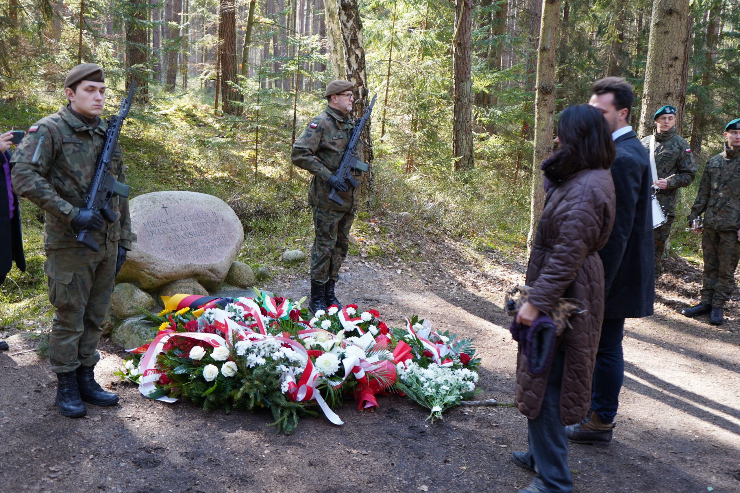 Przedstawiciele władz oraz uczestnicy uroczystości składają wieńce przy kamieniu pamiątkowym, obok stoją żołnierze pełniący wartę honorową