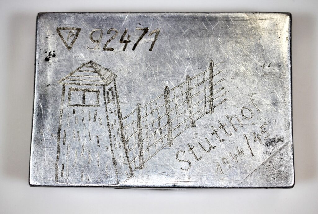 Metalowa papierośnica z wygrawerowanym rysunkiem wieży strażniczej, drutu kolczastego oraz napisem: „P 92471 Stutthof 1944/45”. Widoczne oznaczenie więźnia politycznego i numer obozowy Edmunda Przyklęk.