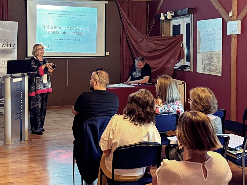 Referat na temat pogranicza polsko-niemieckiego, kobieta prezentuje slajd z tytułem wystąpienia, uczestnicy siedzą w skupieniu.
