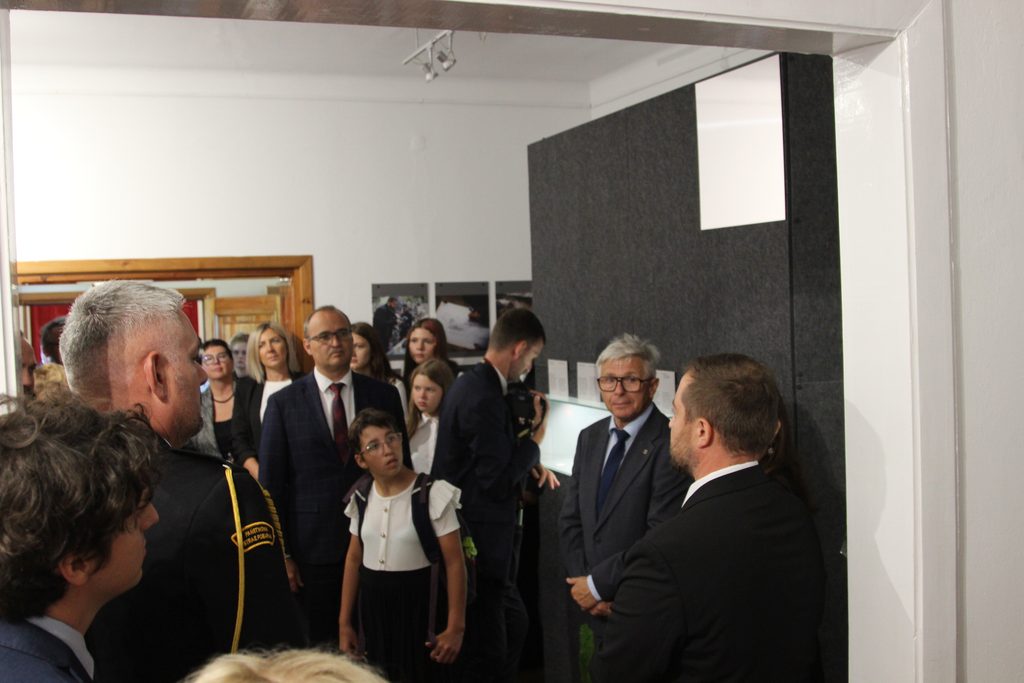 Grupa uczestników zwiedza wystawę Muzeum Stutthof i słucha osoby opowiadającej o prezentowanych eksponatach.