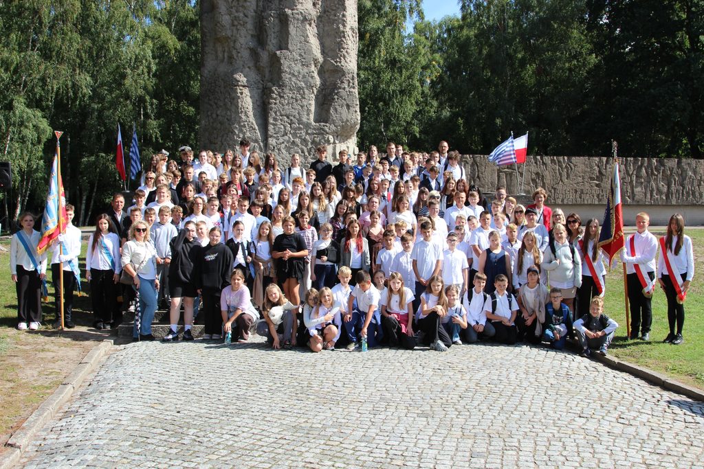 Duża grupa dzieci i młodzieży szkolnej z opiekunami i pocztami sztandarowymi przed Pomnikiem Walki i Męczeństwa.